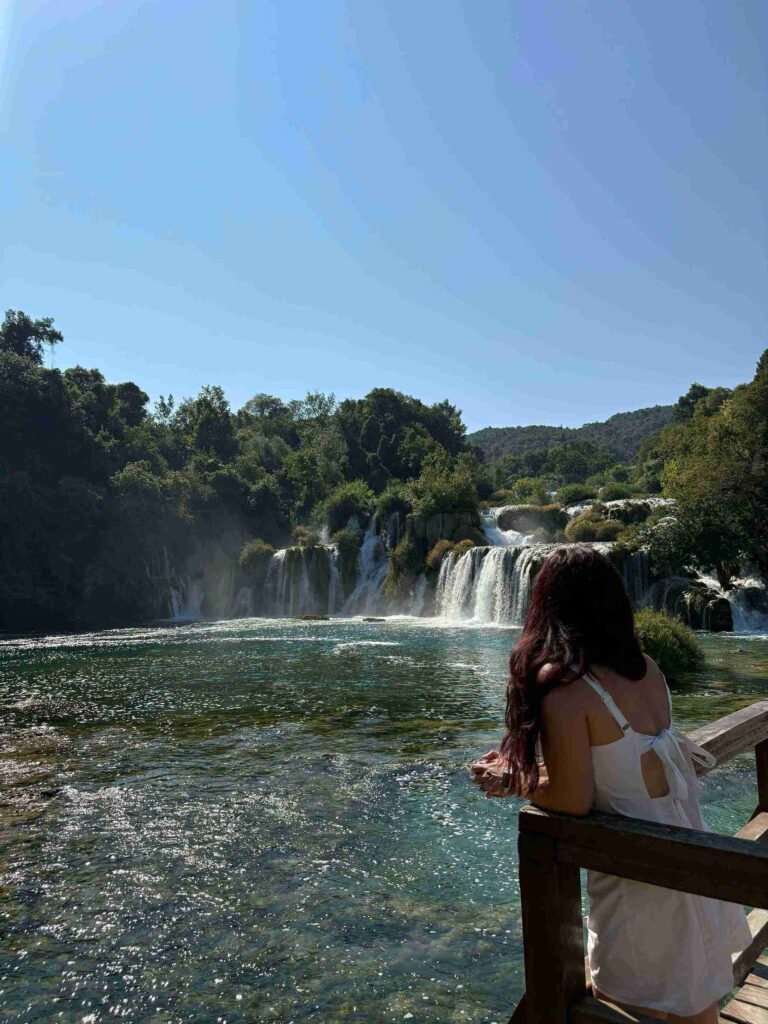 Person standing at a wooden railing looking toward Skradinski Buk waterfalls at Krka National Park, Croatia.