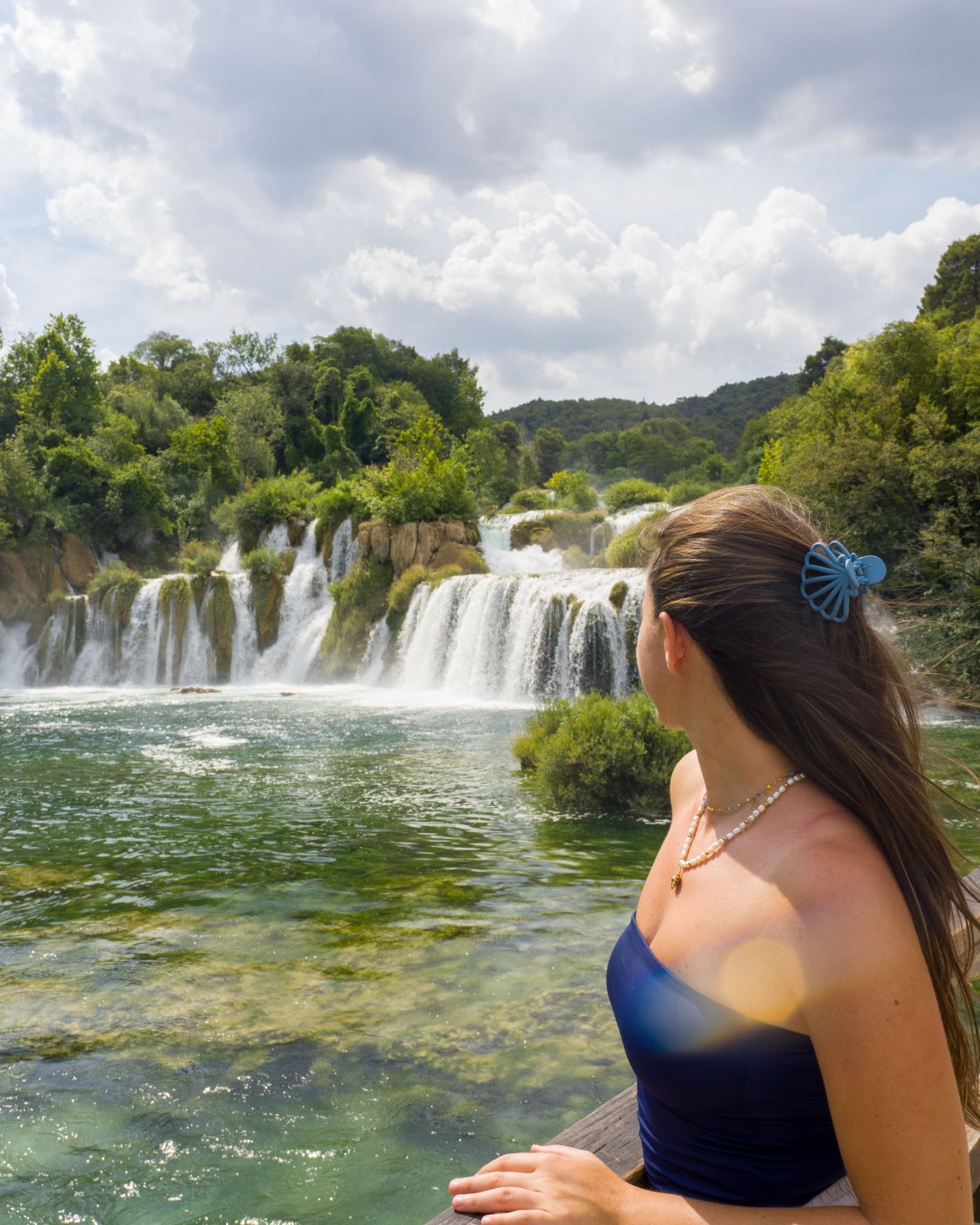 Woman standing on a wooden viewpoint looking at Skradinski Buk waterfalls in Krka National Park, Croatia.