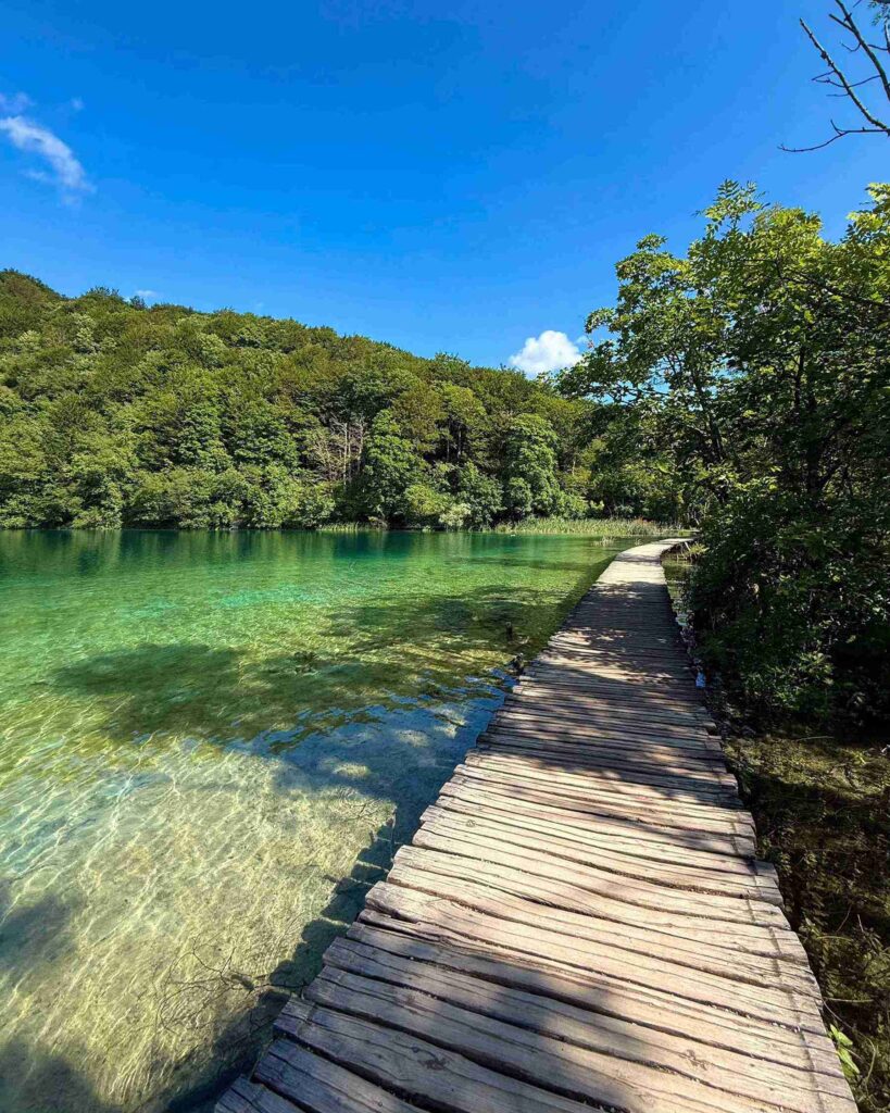 Wooden boardwalk beside crystal-clear turquoise lake at Plitvice Lakes National Park, Croatia.